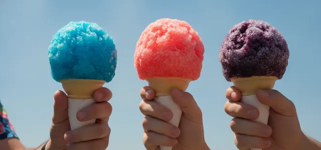 Colorful shaved-ice cones held against a blue sky